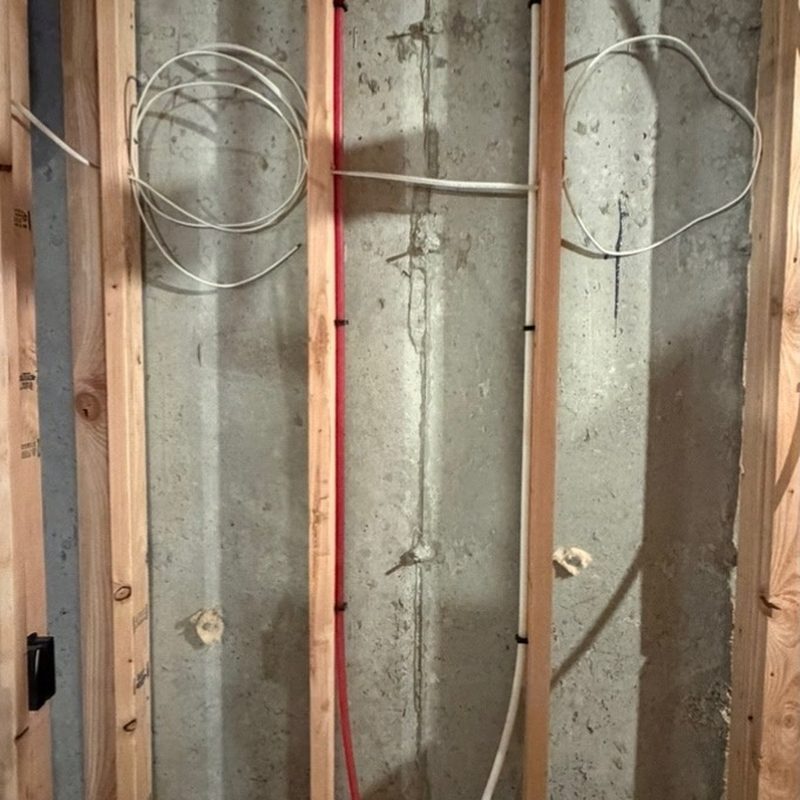 Cable coiled and stapled to new timber studs against a concrete foundation wall.