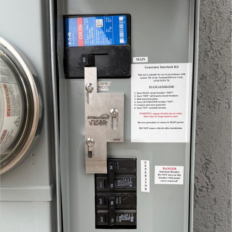 A panel interior with a metal interlock plate over the main breaker, beside a printed instruction placard.