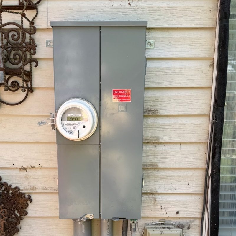 A new grey meter main enclosure with a red emergency disconnect label, fed by conduit riser out of the ground.